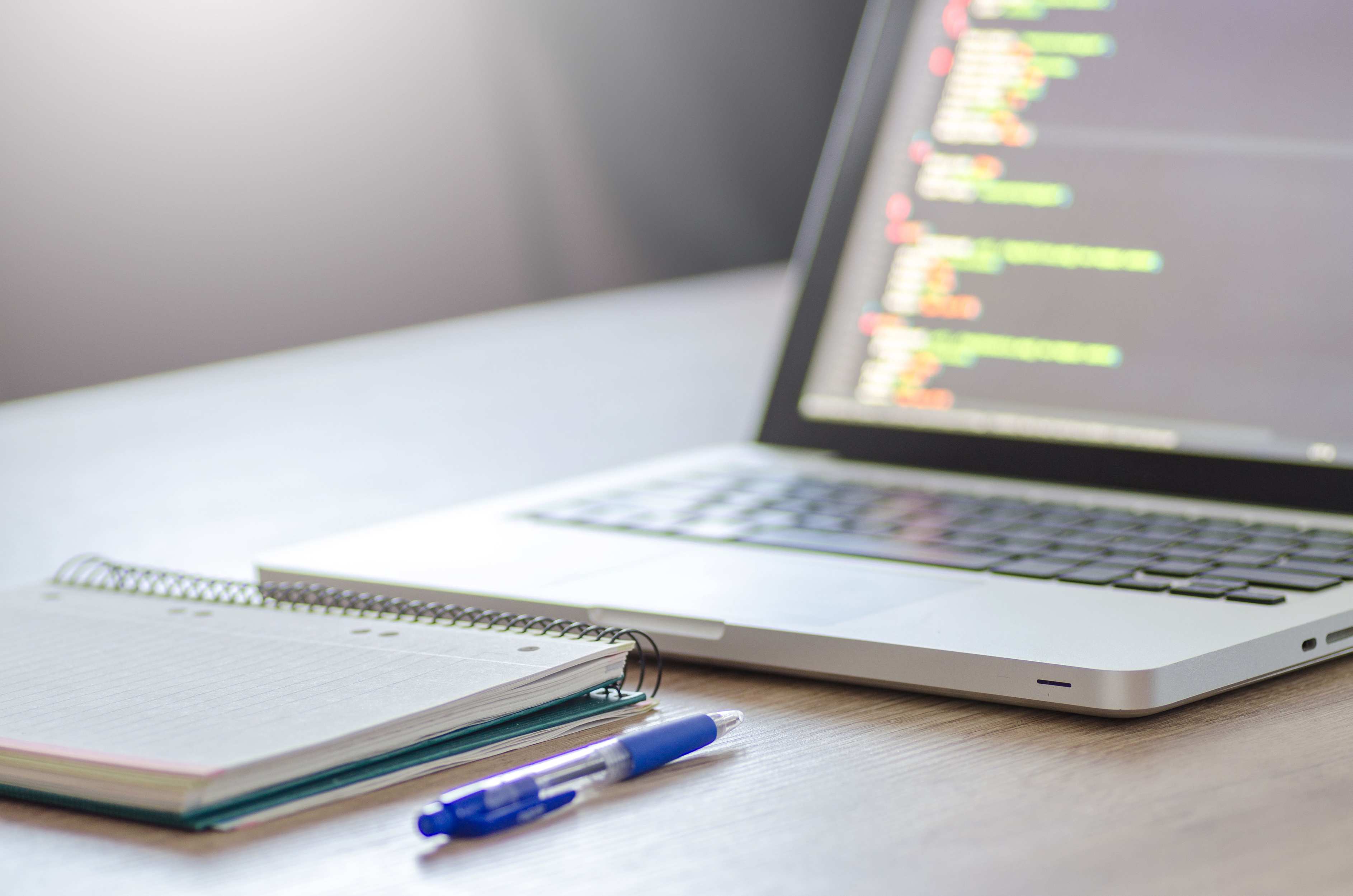 Wide view of a laptop on a desk in a modern workspace with programming code on screen